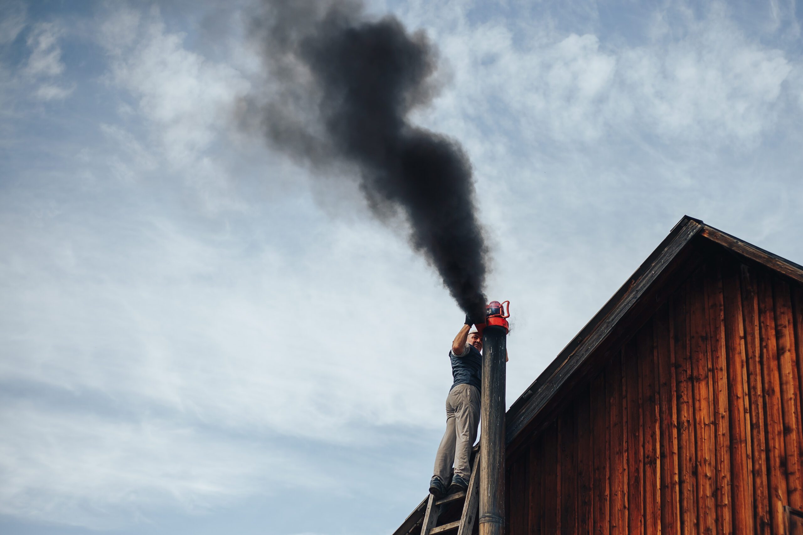 Chimney sweep cleaning a chimney standing balanced on the apex of a house roof lowering equipment down the flue