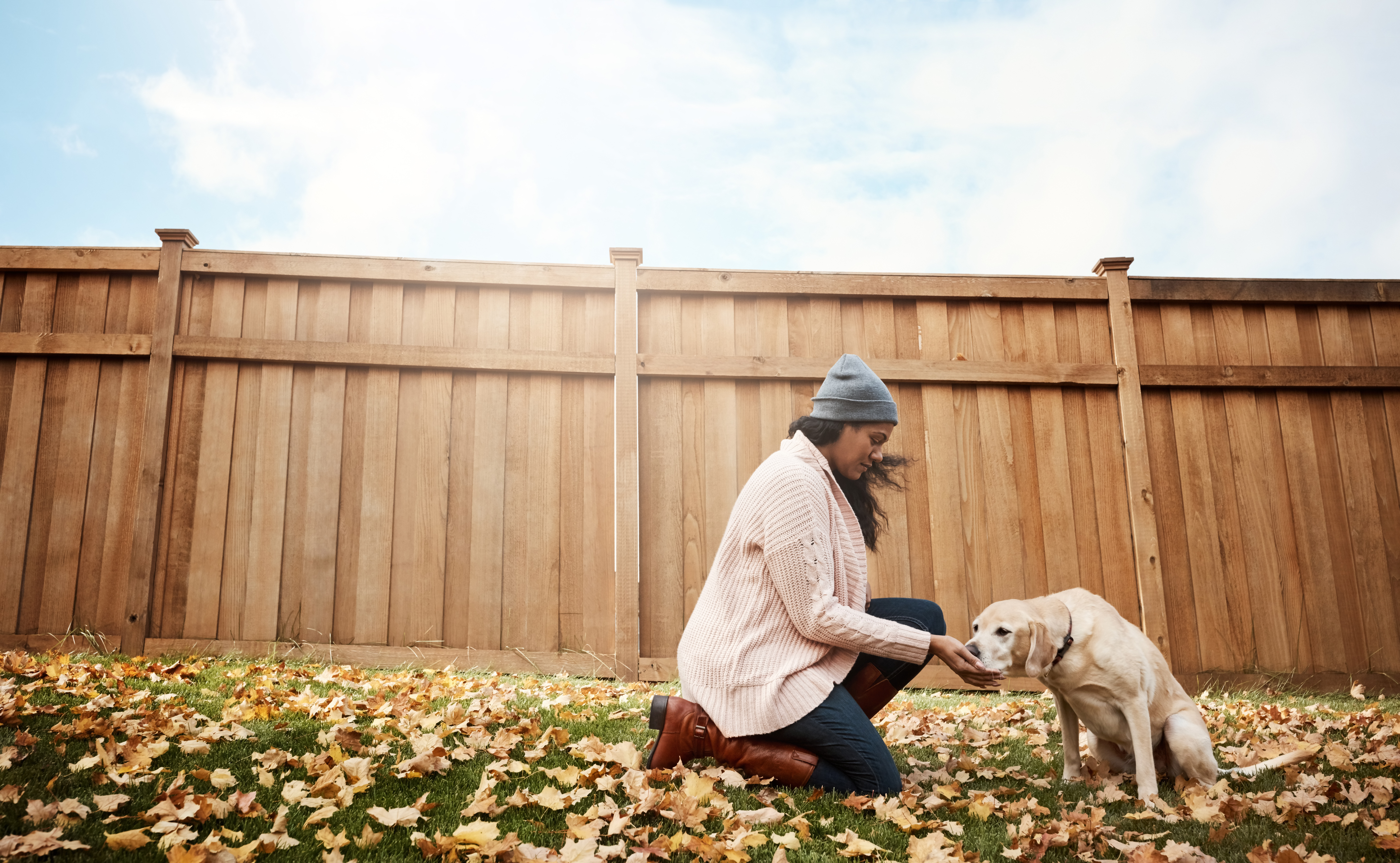 a woman outside in the fall in front of a new wood built fence with a dog