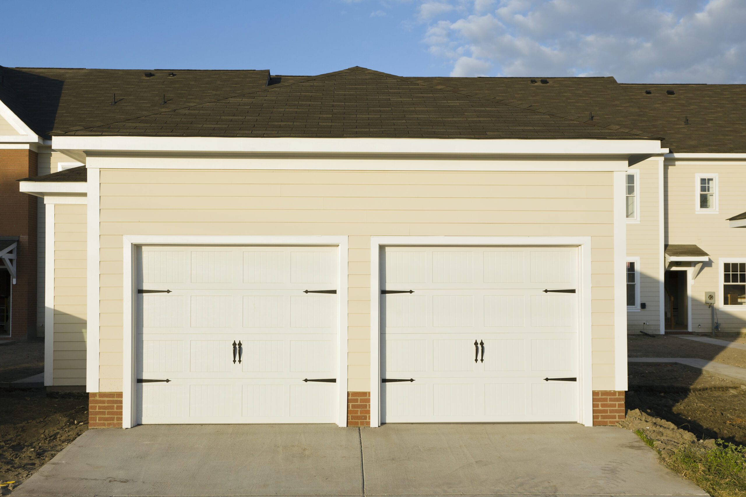 Beige townhouse with two white paneled garage doors featuring decorative black hardware.