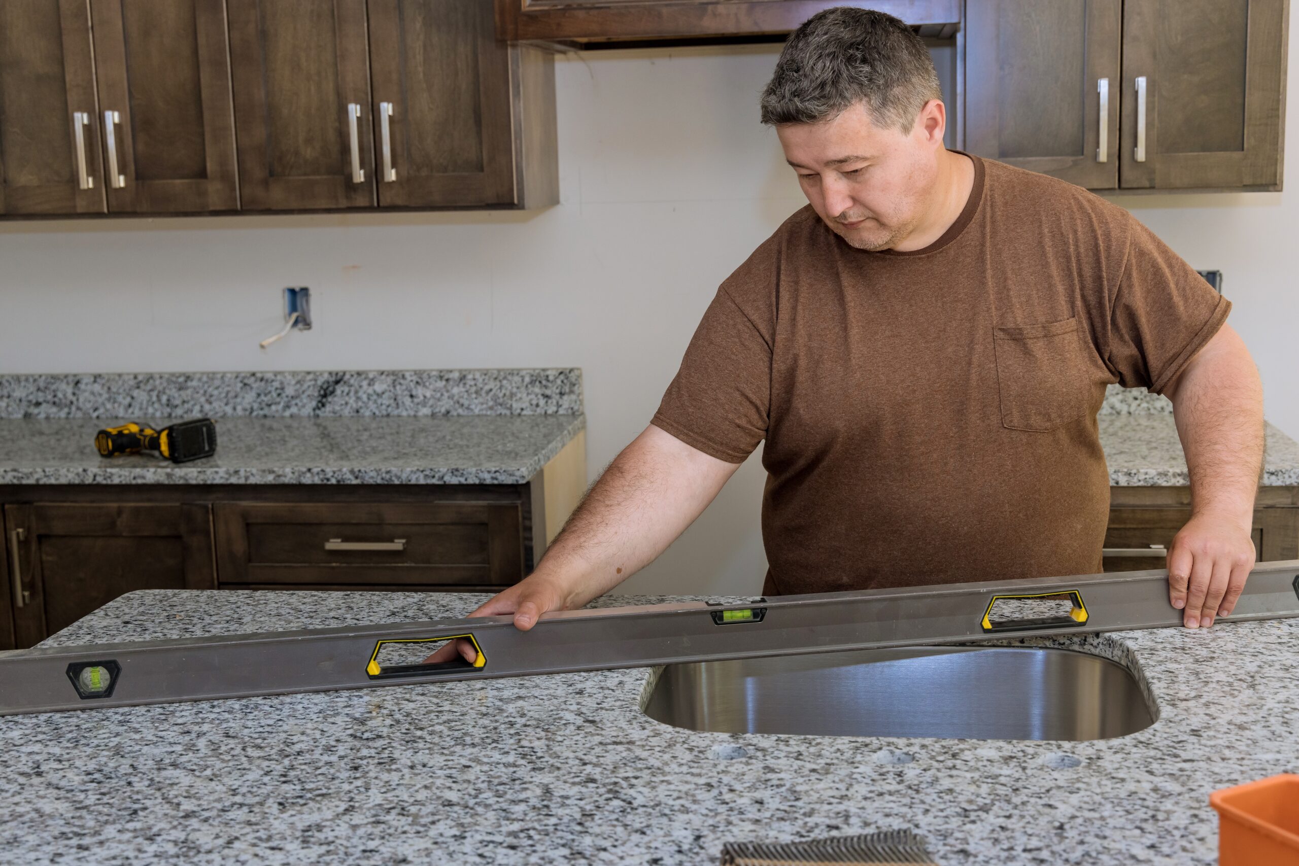 Man using a level to ensure precise granite countertop installation in kitchen remodeling project