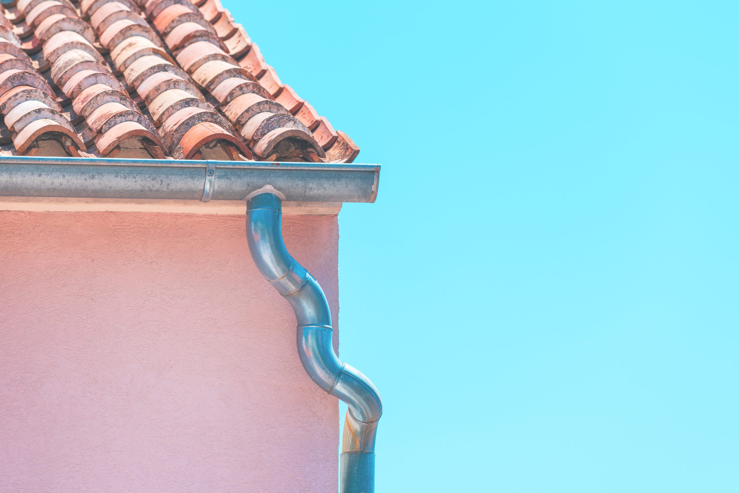 Galvanized steel rain gutter and clay tile roof on pink stucco Mediterranean-style home