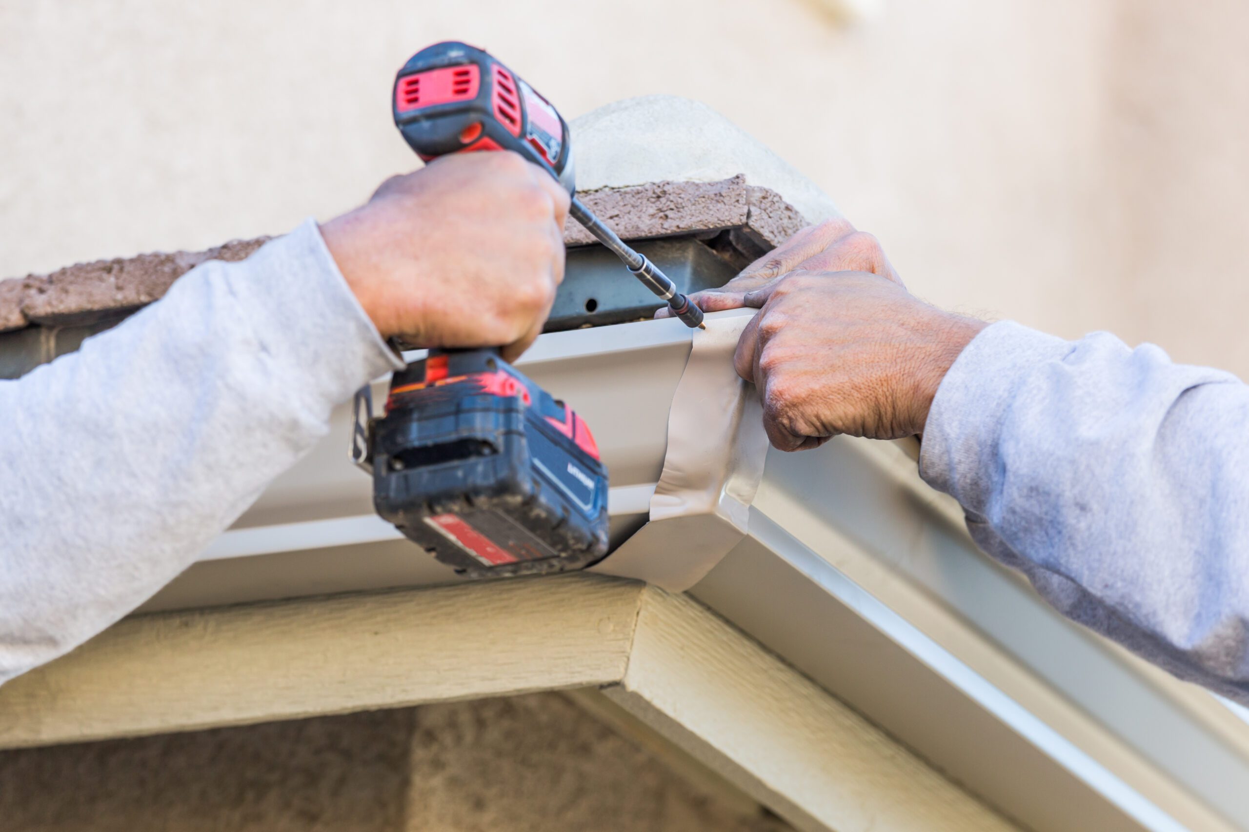 Close-up of workers attaching aluminum gutter to fascia board with drill