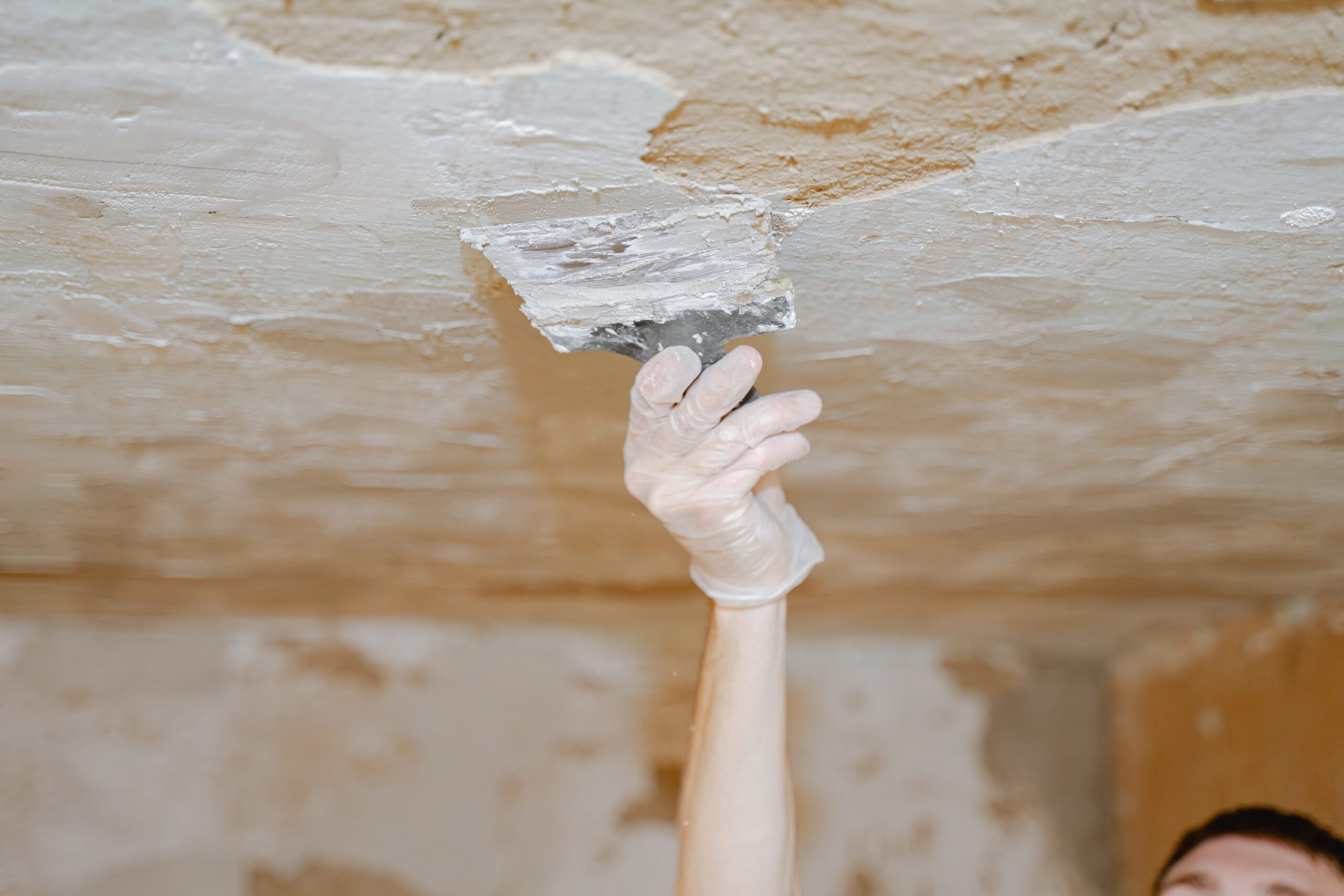 Hand with putty knife applying patch to textured ceiling