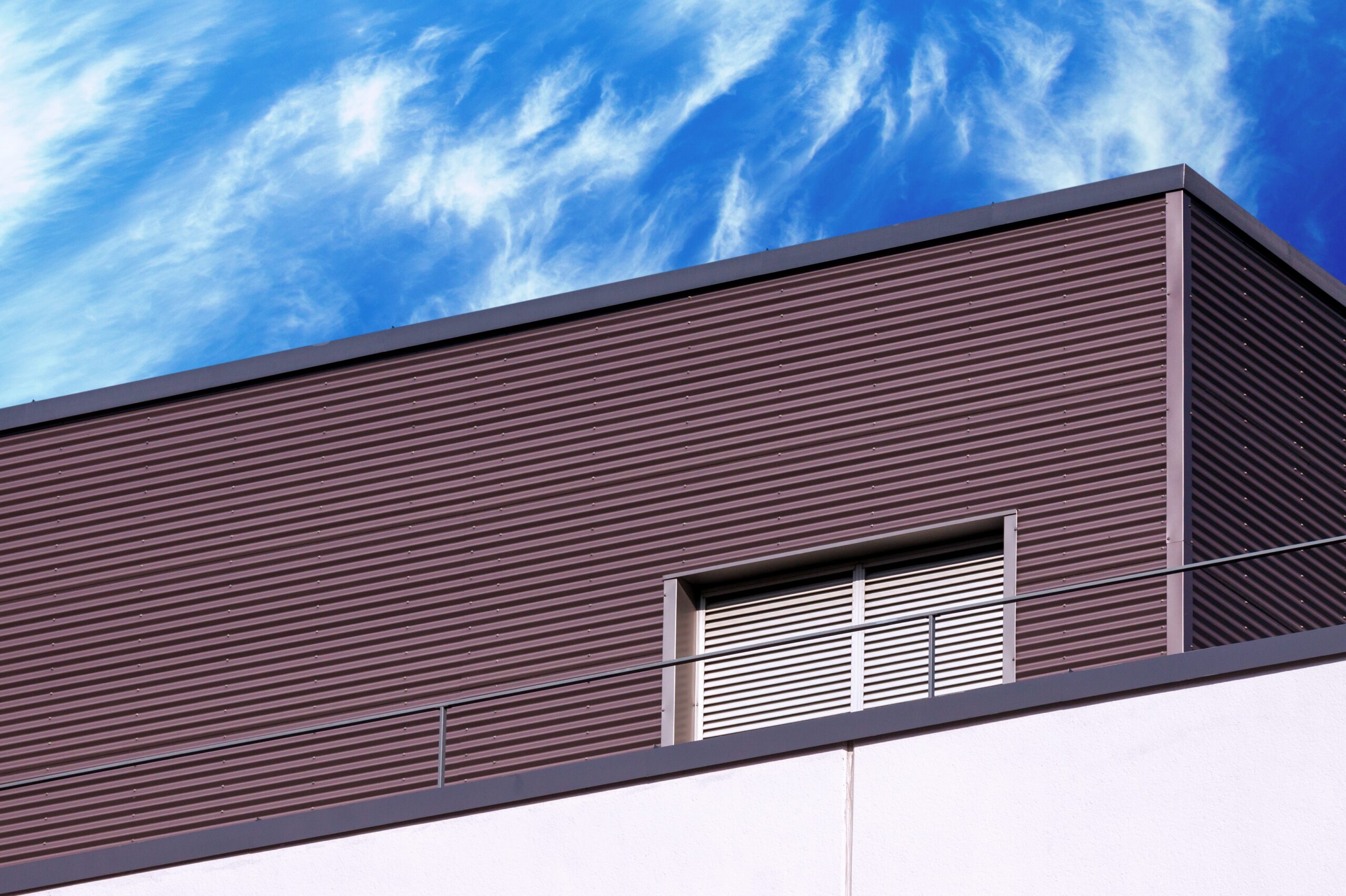 Siding Installation on Modern Building - LBJ Roofing Company Corp. Brown metal siding installation on commercial building under blue sky