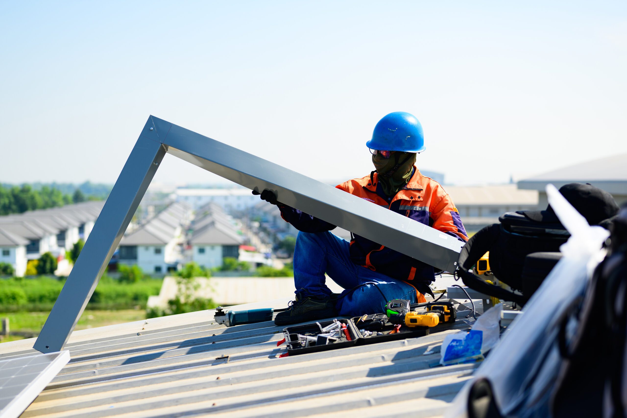 Technician in safety gear working on metal roofing installation with tools and materials on rooftop