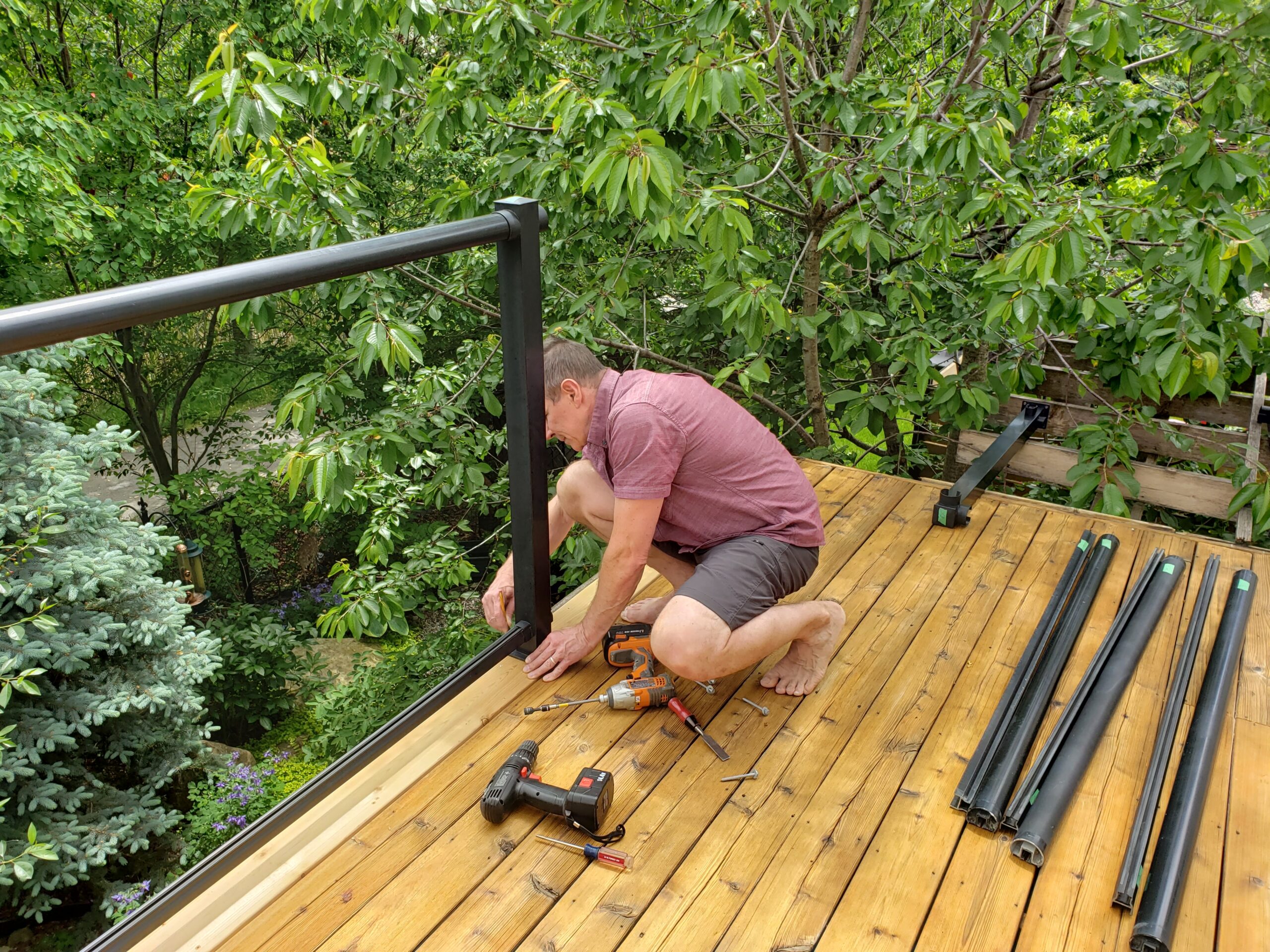 Deck Upgrade Highlighting Porch Services Results - LBJ Roofing Company Corp. Man working on a deck railing surrounded by greenery, showcasing results of quality porch services.