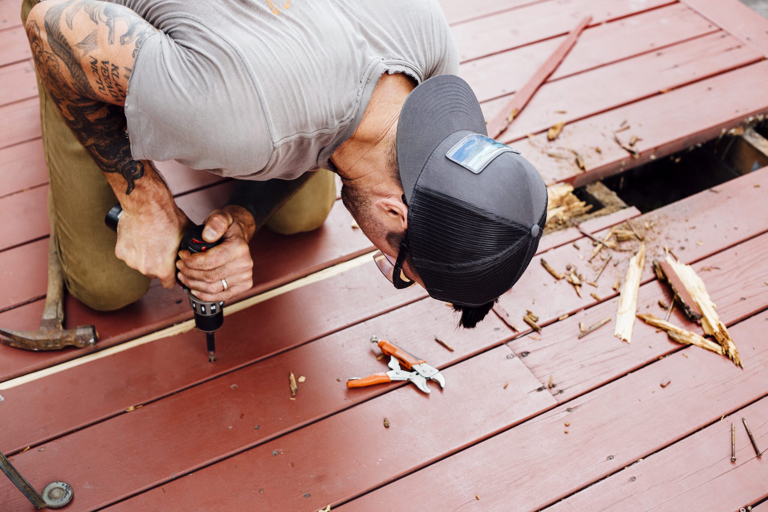 Homeowner Repairing Deck with Help from Porch Services - LBJ Roofing Company Corp. Man drilling into red wooden decking during a repair project supported by expert porch services.