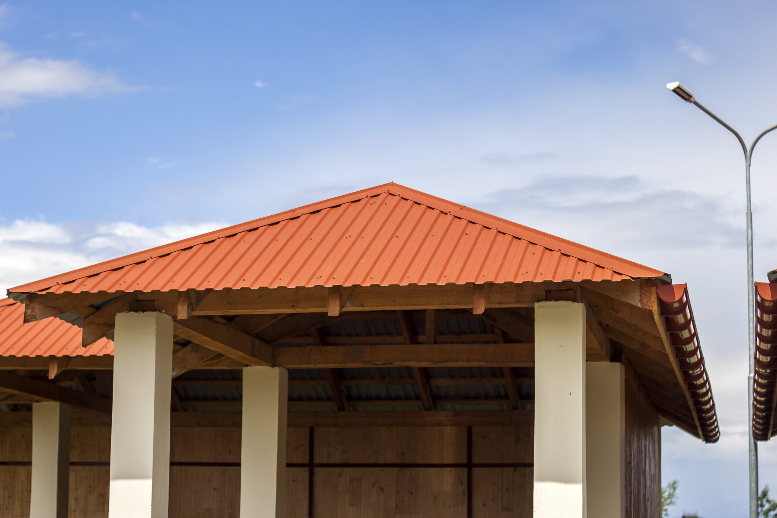 Open pavilion structure featuring vibrant red corrugated metal roofing under a clear sk