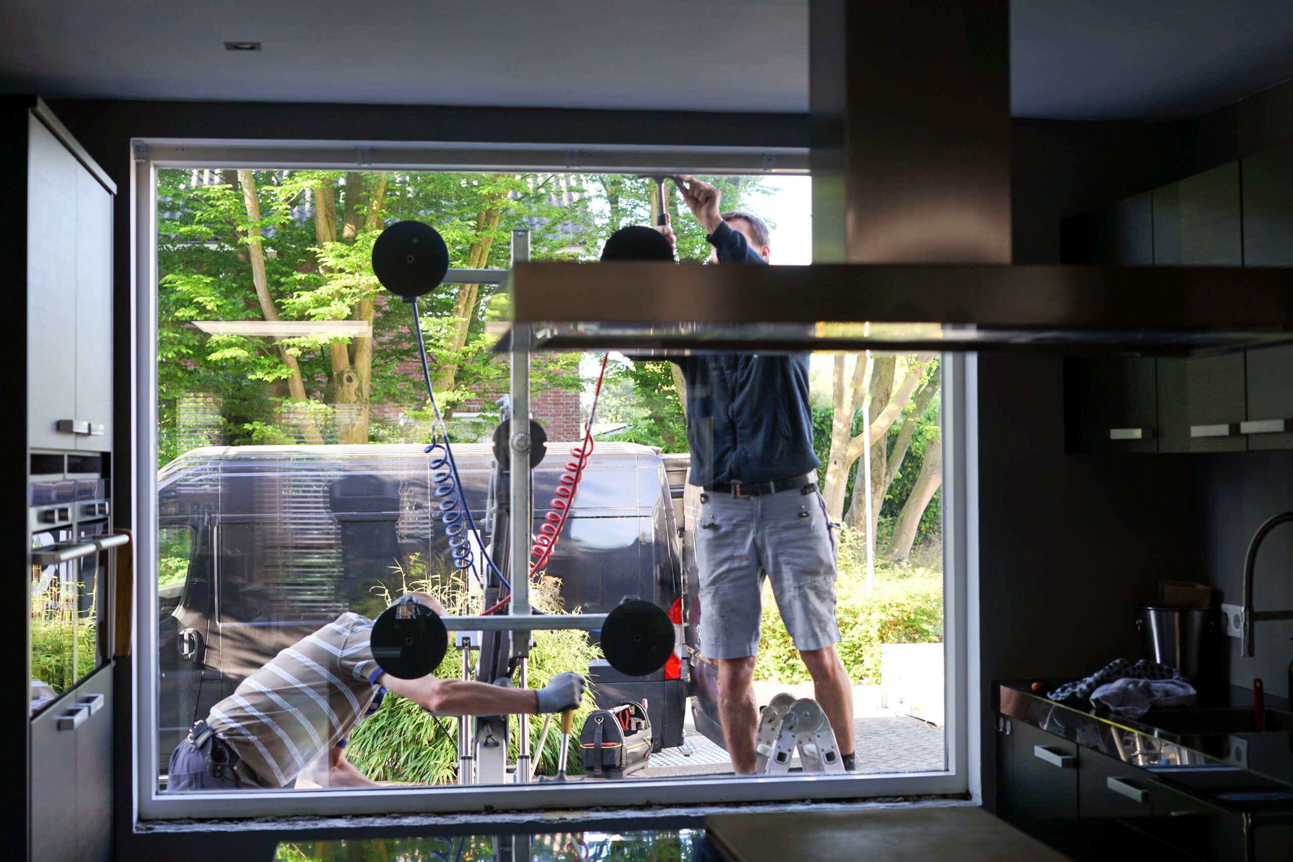 Large Glass Window Installation in Kitchen - LBJ Roofing Company Corp. Workers installing large glass window viewed from inside a modern kitchen